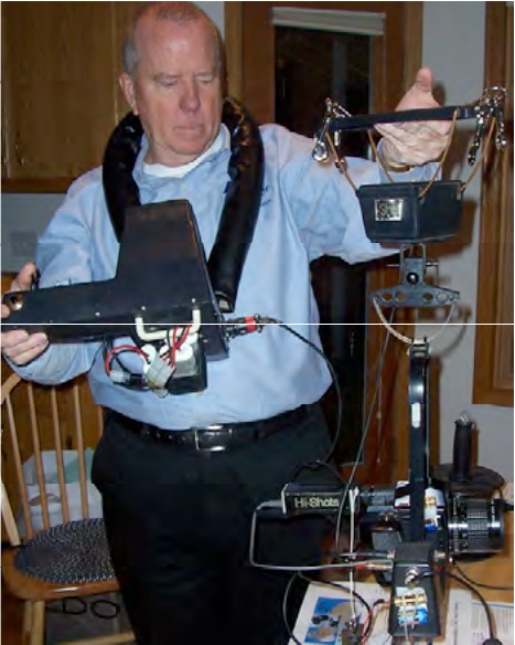 Bill James wearing a neck-harness control display, holding a test rig with a camera and three coaxially mounted lasers.